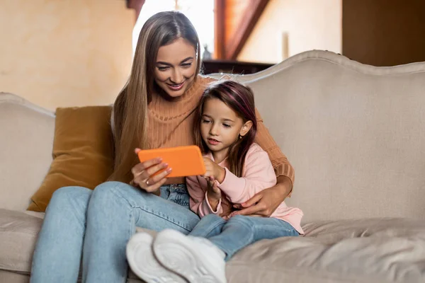 Portrait of smiling mom and girl using smartphone at home — Stock Photo, Image