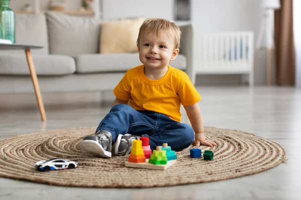 Roztomilý batole chlapec hraje s autem a vzdělávací dřevěné hračky doma, sedí na podlaze koberec v obývacím pokoji a usmívá — Stock fotografie