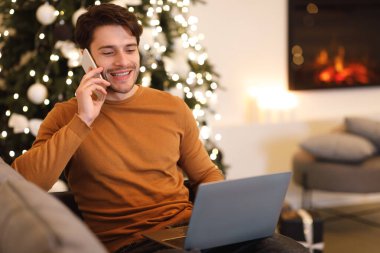 Cep telefonuyla konuşan neşeli bir adam bilgisayar kullanıyor.