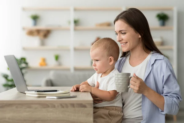 Jeune mère avec petit bébé buvant du café et utilisant un ordinateur portable à la maison — Photo