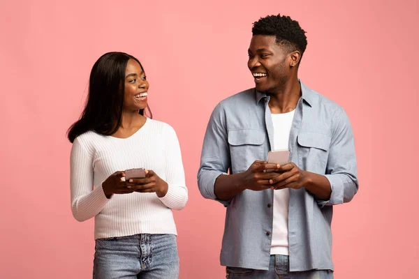 Cheerful man and woman with smartphones looking at each other