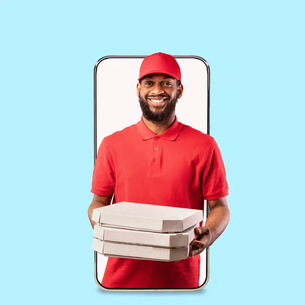 Alegre joven negro repartidor en uniforme da un montón de cajas de pizza de pantalla en blanco de teléfono grande — Foto de Stock