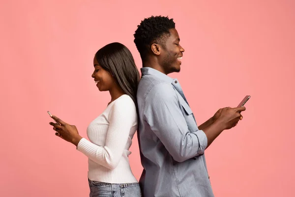 Pasangan kulit hitam positif berdiri dari belakang ke belakang, menggunakan smartphone — Stok Foto