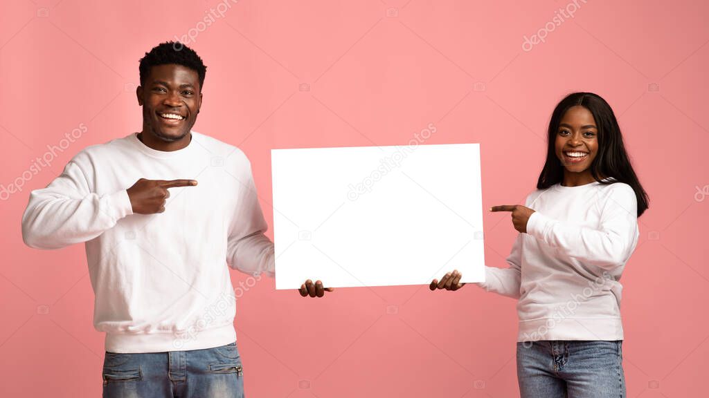 Happy black couple pointing at advertising board in their hands