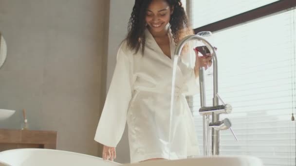 After work relax. Young african american lady enjoying wine glass and taking water into bathtub at home, tracking shot — Stock Video