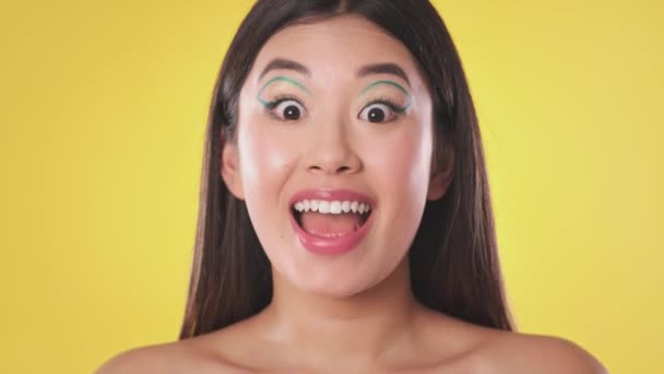 Ung vacker asiatisk kvinna med kreativ makeup ropar OMG, chockad över att höra om enorm försäljning, gul bakgrund — Stockvideo