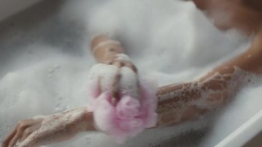 Genç Afrikalı Amerikalı kadın, sünger ve sabunla vücudunu yıkıyor, evde sabun banyosu yapıyor, çekimleri takip ediyor.
