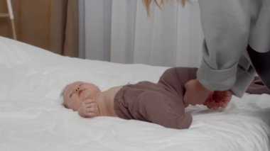 Bakıcı anne, yeni doğmuş bebeğini evde yatakta giydiriyor.