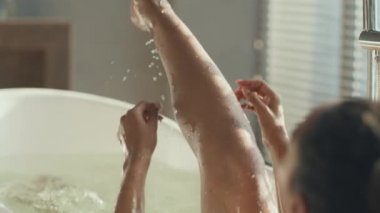 Tanımlanamayan Afro-Amerikalı bayan sıcak bir banyoda dinleniyor, bacağını kaldırıyor ve okşuyor.