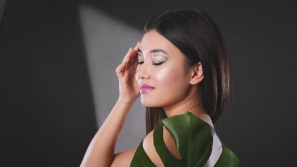 Selbstliebe und Fürsorge. Junge asiatische Frau mit kreativem Make-up bedeckt Körper mit Monstera Blatt und streichelt perfekte Haut — Stockvideo