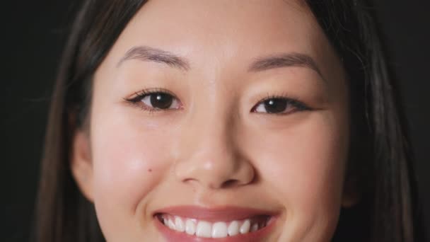 Wellbeing concept. Close up portrait of young cheerful asian lady smiling to camera over black studio background — Stock Video