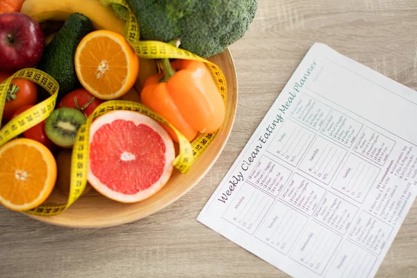 Planificador de comidas semanal y plato de frutas y verduras frescas cerca en la mesa — Foto de Stock