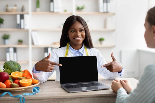 Aplicación o sitio web para la dieta. Nutricionista afroamericana mostrando pantalla de computadora portátil en blanco paciente para maqueta —  Fotos de Stock