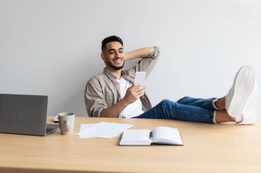 Arap adam cep telefonu kullanarak ayaklarını masaya koyuyor.