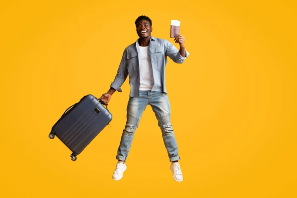 Емоційний афроамериканський хлопець з валізою і квитками на літак стрибає — стокове фото