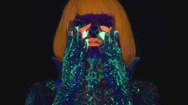 Schoonheid mode portret van jonge vrouw in oranje pruik met neon body art schilderij fluorescerende verf op haar gezicht en nek — Stockvideo