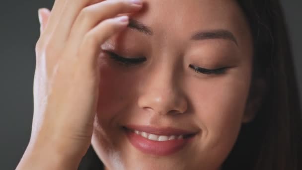 Schönheits- und Wellness-Konzept. Junge gepflegte schüchterne asiatische Frau flirtet vor der Kamera, fixiert ihre Haare und lächelt, Nahaufnahme — Stockvideo