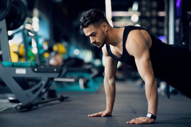 Spor salonunda antrenman yapan kaslı Arap adam şınav çekiyor.