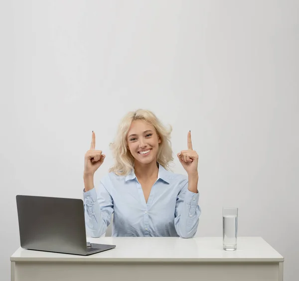 Glückliche Geschäftsfrau sitzt mit Laptop am Schreibtisch und zeigt mit dem Finger auf Kopierraum auf hellem Studiohintergrund, Schnitte — Stockfoto