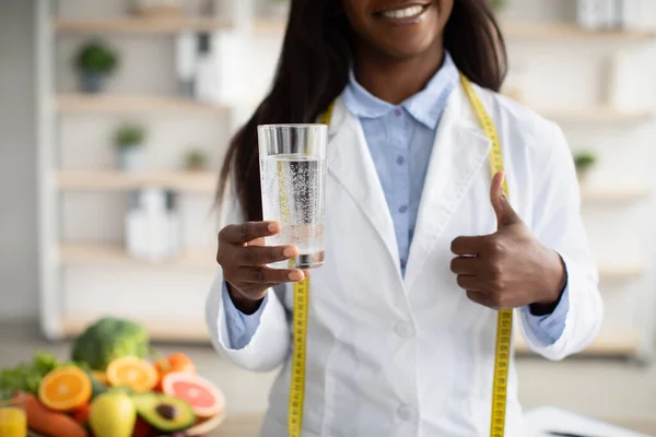Detox e concetto di pulizia. Nutrizionista afroamericana che tiene un bicchiere d'acqua e mostra il pollice in alto — Foto Stock