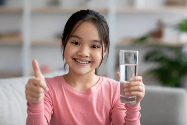 Positivt kinesisk barn med vannglass som viser tommelen opp – stockfoto