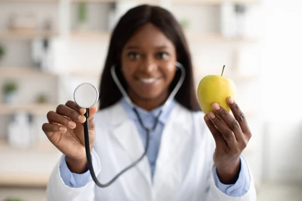 Nutrizionista afroamericano che mostra mela verde biologica e utilizza stetoscopio, primo piano — Foto Stock