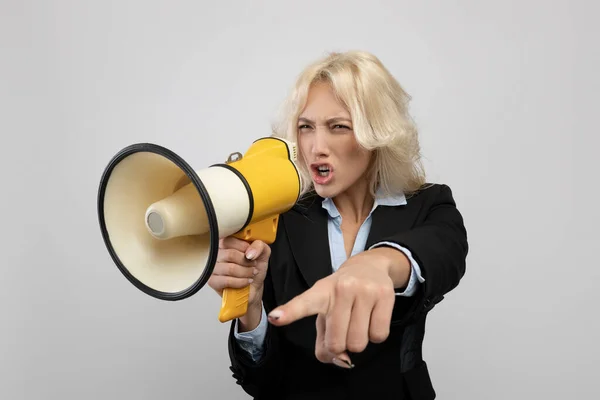 Empresária agitada em roupa formal gritando em megafone e apontando o dedo, posando em fundo cinza — Fotografia de Stock