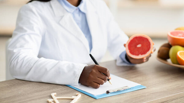 African american female nutritionist holding grapefruit, making meal plan for client at weight loss clinic, closeup