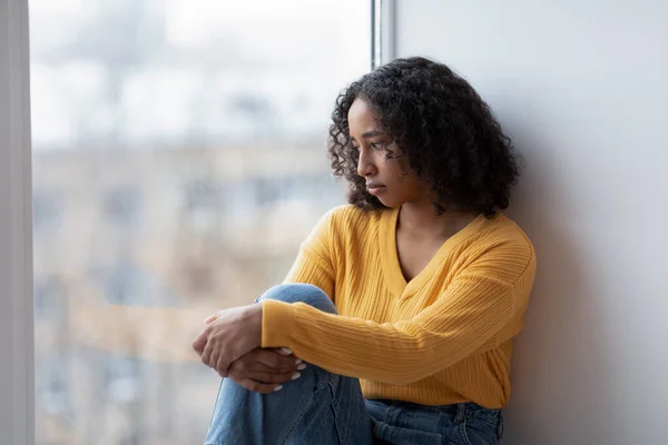 Mujer negra joven infeliz mirando por la ventana, teniendo pensamientos depresivos en casa, espacio de copia —  Fotos de Stock