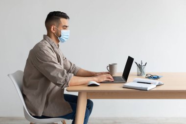 Koruyucu maskeli bir adam merkez büroda bilgisayar üzerinde çalışıyor.