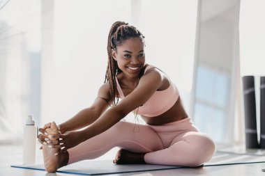 Spor giyimli, mutlu, genç bir zenci kadın vücudunu uzatıyor.