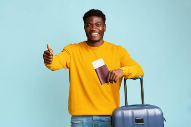 Uçak biletleri ve pasaportu olan siyah bir adam mavi üzerine izole edilmiş.