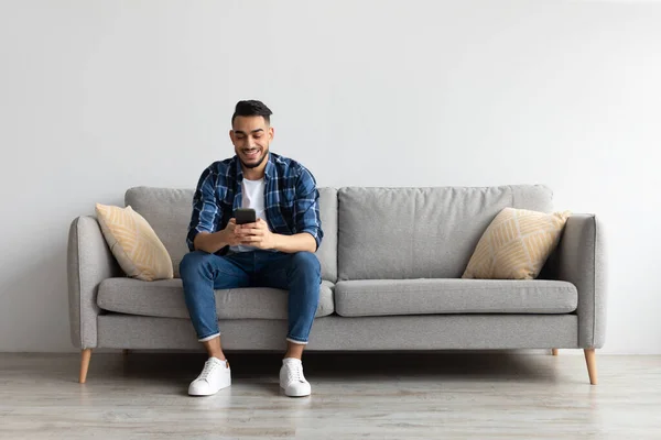 Retrato del hombre árabe sonriente usando un teléfono inteligente en casa —  Fotos de Stock