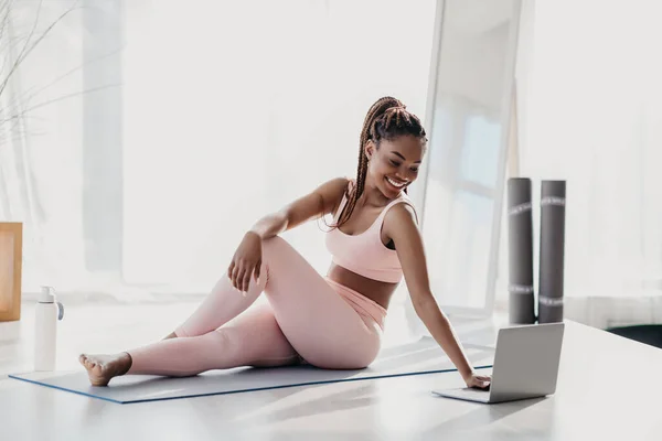 Positivo hermosa milenaria mujer afroamericana en ropa deportiva haciendo estiramiento delante de la computadora portátil en casa —  Fotos de Stock