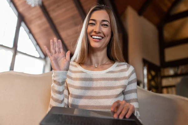 Smiling adult lady using pc laptop waving hand to camera