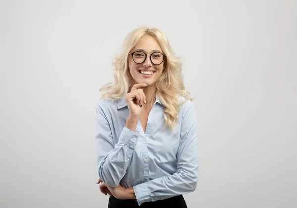 Una carriera da donna d'affari. Positivo giovane donna d'affari toccando mento e sorridendo alla fotocamera, in piedi su sfondo chiaro — Foto Stock