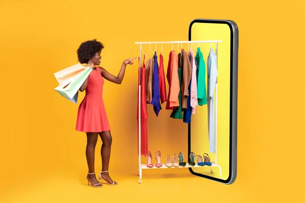 Nero signora shopping scelta vestiti in enorme telefono, sfondo giallo — Foto Stock