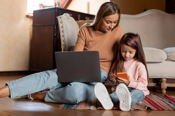 Happy woman and daughter using laptop and cellphone — Stock Photo, Image