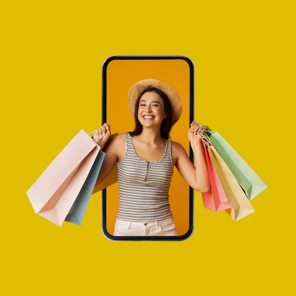 Shopaholic signora nello schermo del telefono che tiene borse della spesa, sfondo giallo — Foto Stock
