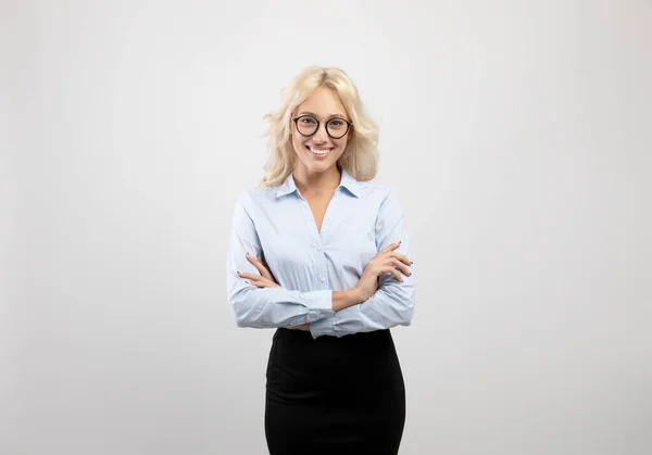 Felice giovane donna d'affari in abito formale e occhiali in piedi con le braccia incrociate su sfondo grigio chiaro studio — Foto Stock