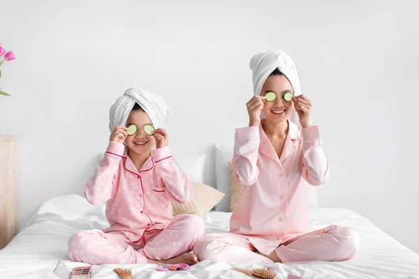 Feliz asiático adolescente menina e jovem mulher se divertir, aplicar fatias de pepino aos olhos, sentar na cama com cosméticos — Fotografia de Stock