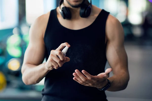 Unerkennbarer muskulöser Mann trägt vor dem Training im Fitnessstudio Desinfektionsspray auf die Hände auf — Stockfoto