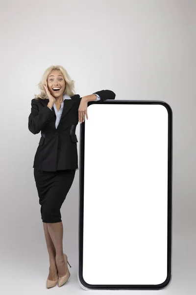 App de negócios. Empreendedora mulher entusiasmada em desgaste formal inclinando-se em grande smartphone em branco com tela branca, mockup — Fotografia de Stock