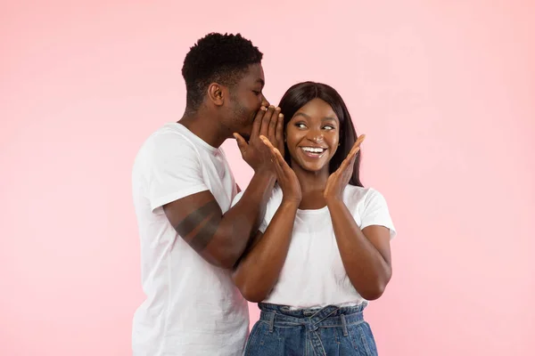Zwarte man delen van nieuws met opgewonden vrouw fluisteren naar oor — Stockfoto