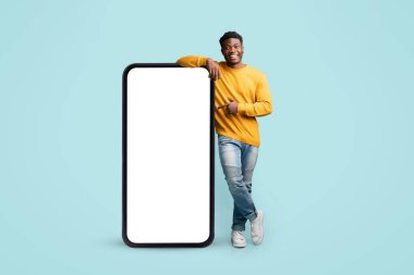 Neşeli siyah adam boş ekranlı büyük akıllı telefonun yanında duruyor.