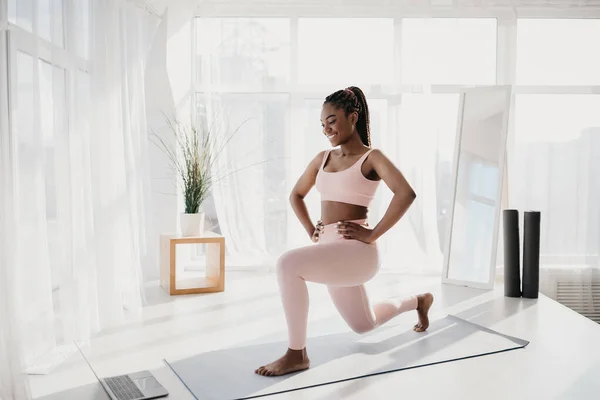 Junge schwarze Frau macht Ausfallschritt, macht Kraftübungen, trainiert zu Hause zu Online-Sportanleitung, leerer Raum — Stockfoto