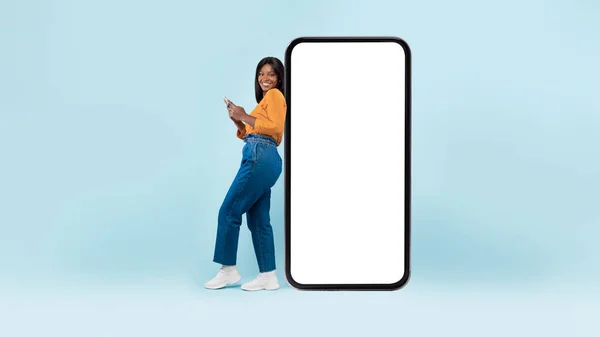 Mulher negra apoiando-se na tela do smartphone branco vazio, usando celular — Fotografia de Stock