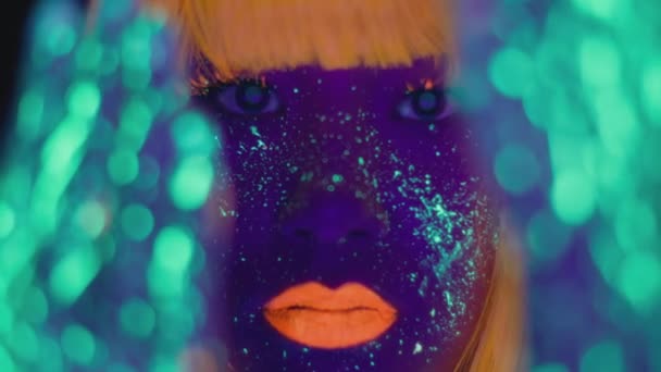 Ung kvinna med ljusa fluorescerande makeup och kroppskonst poserar till kameran, gester med glödande händer, selektivt fokus — Stockvideo
