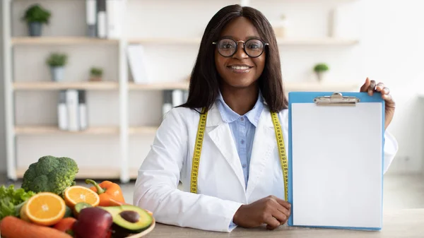 Médecin nutritionniste afro-américain tenant un presse-papiers vierge, montrant une maquette pour le menu nutritionnel droit, espace de copie — Photo