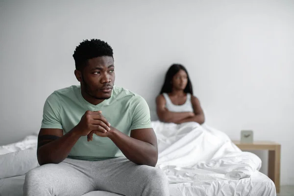 Deprimido triste joven negro hombre ignora ofendido dama después de disputa se sienta en la cama en el interior del dormitorio, espacio de copia —  Fotos de Stock